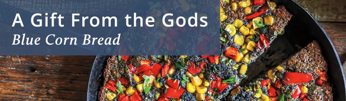 Banner with the title 'A Gift From the Gods' and subtitle 'Blue Corn Bread' over a blue overlay, with colorful corn bread slices in a skillet on the right.
