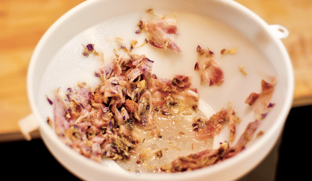 White cup contains a floral herbal tea with dried pink petals floating in milky liquid.