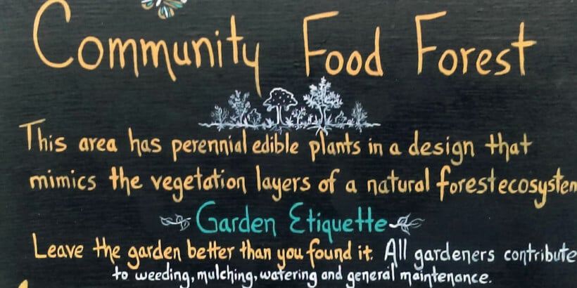 A black sign that says community food forest
