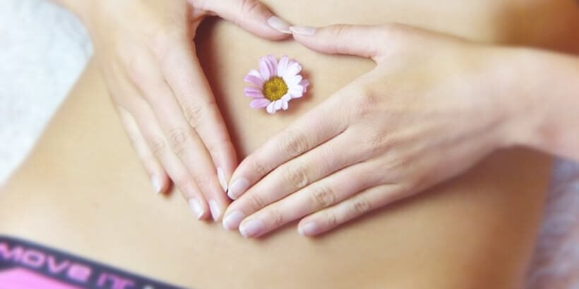 Hands creating heart on bare stomach with a flower in the middle