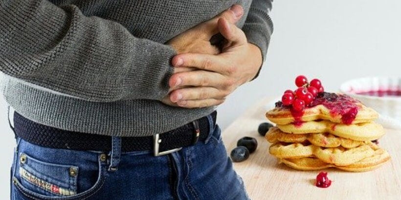 man holding stomach next to pancakes on counter