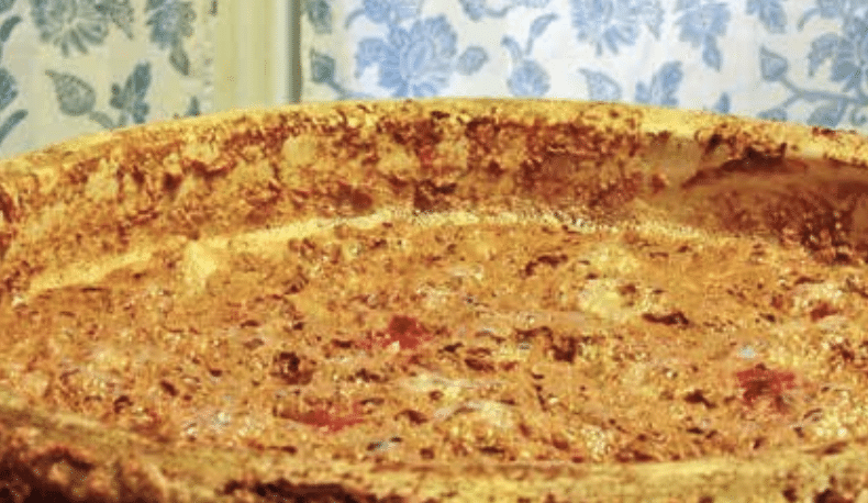 Close-up of a golden-brown baked pie with a bubbly crust and a floral blue wallpaper background.